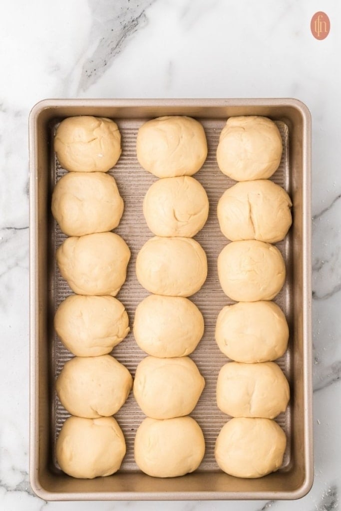 unbaked dinner rolls on a gold baking pan.