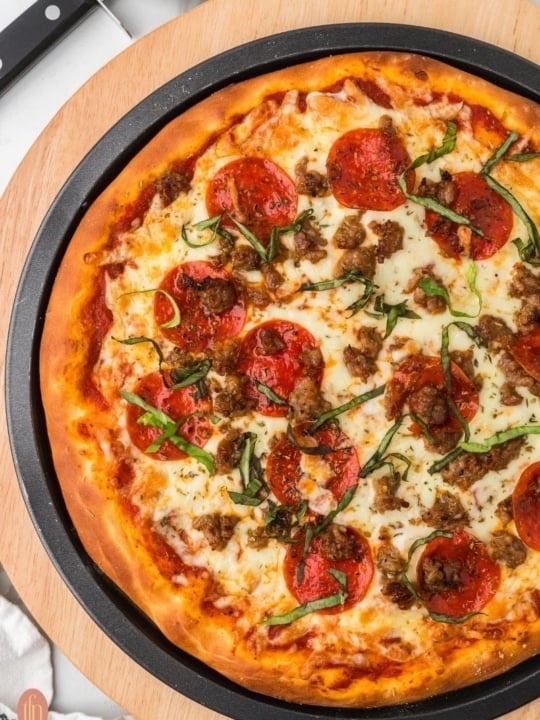 pizza topped with pepperonis, sausage and cheese served on a black circular pan placed on a wooden board.