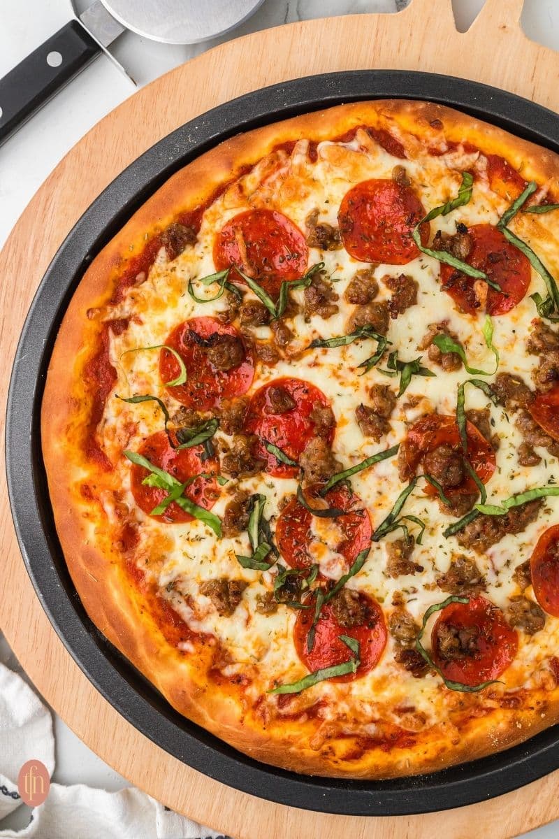 pizza topped with pepperonis, sausage and cheese served on a black circular pan placed on a wooden board.