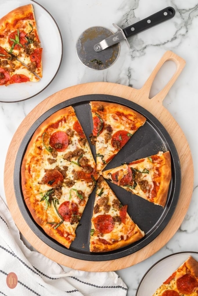 an image of pepperoni and sausage pizza on a black round pan and a stainless steel pizza cutter.