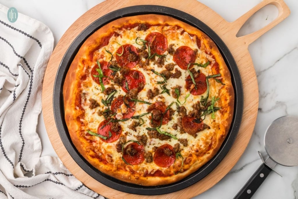 pizza topped with pepperonis and cheese served on a black circular pan placed on a wooden board.