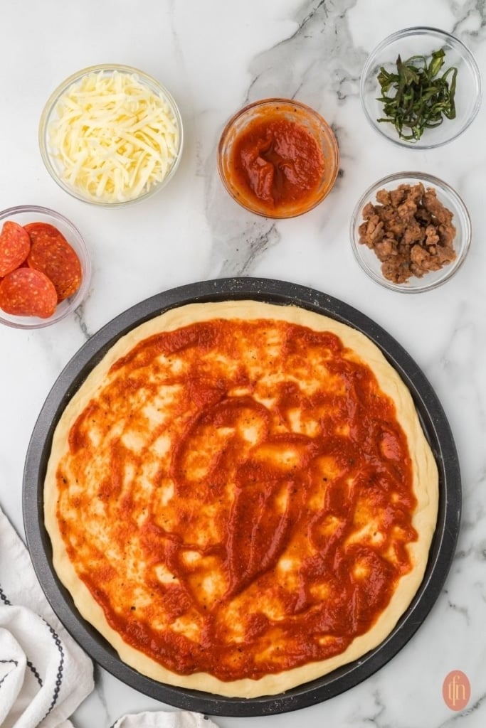 a pizza dough with pizza sauce and other toppings on the side.