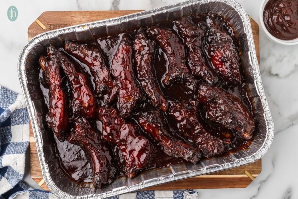 smoked party ribs in a rectangular aluminum foil pan.
