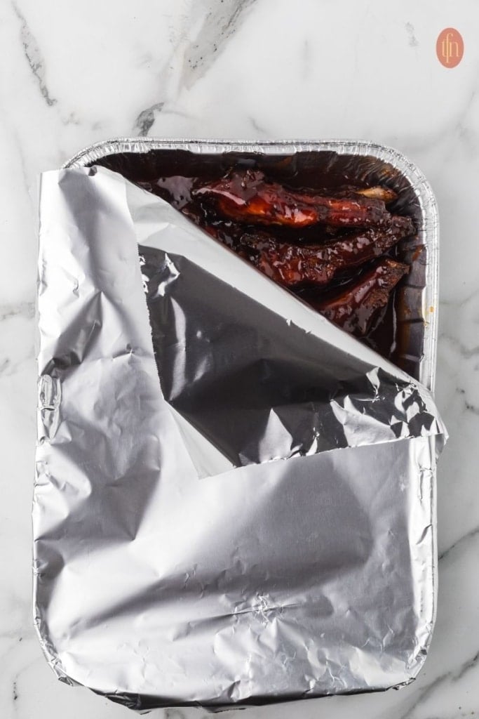 smoked party ribs in a rectangular aluminum foil pan.