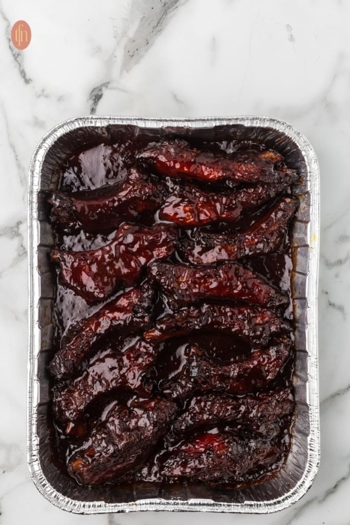 smoked party ribs in a rectangular aluminum foil pan.