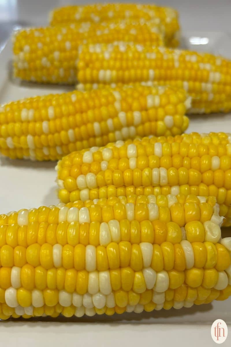 corn on the cob resting on a white serving tray.
