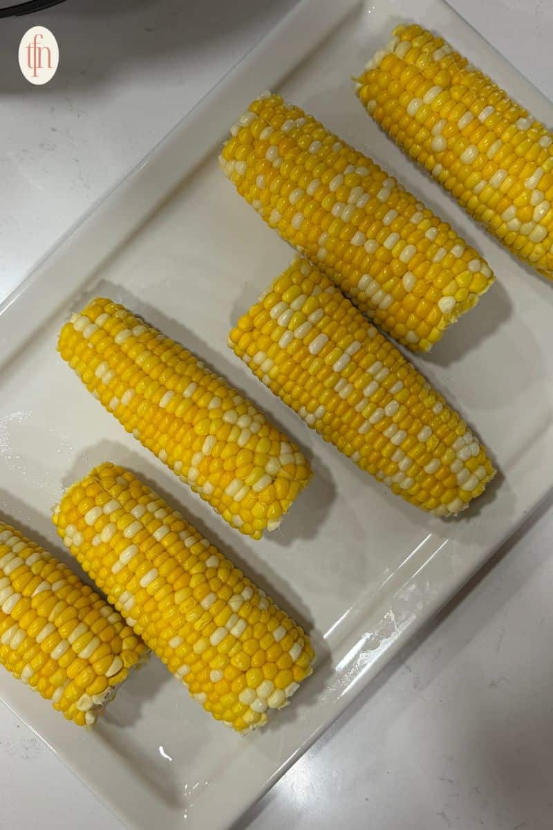 corn on the cob resting on a white serving tray.