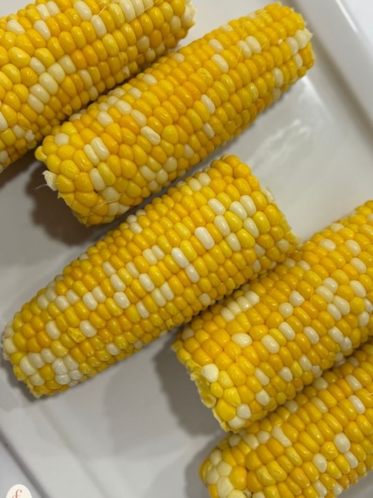 corn on the cob resting on a white serving tray.