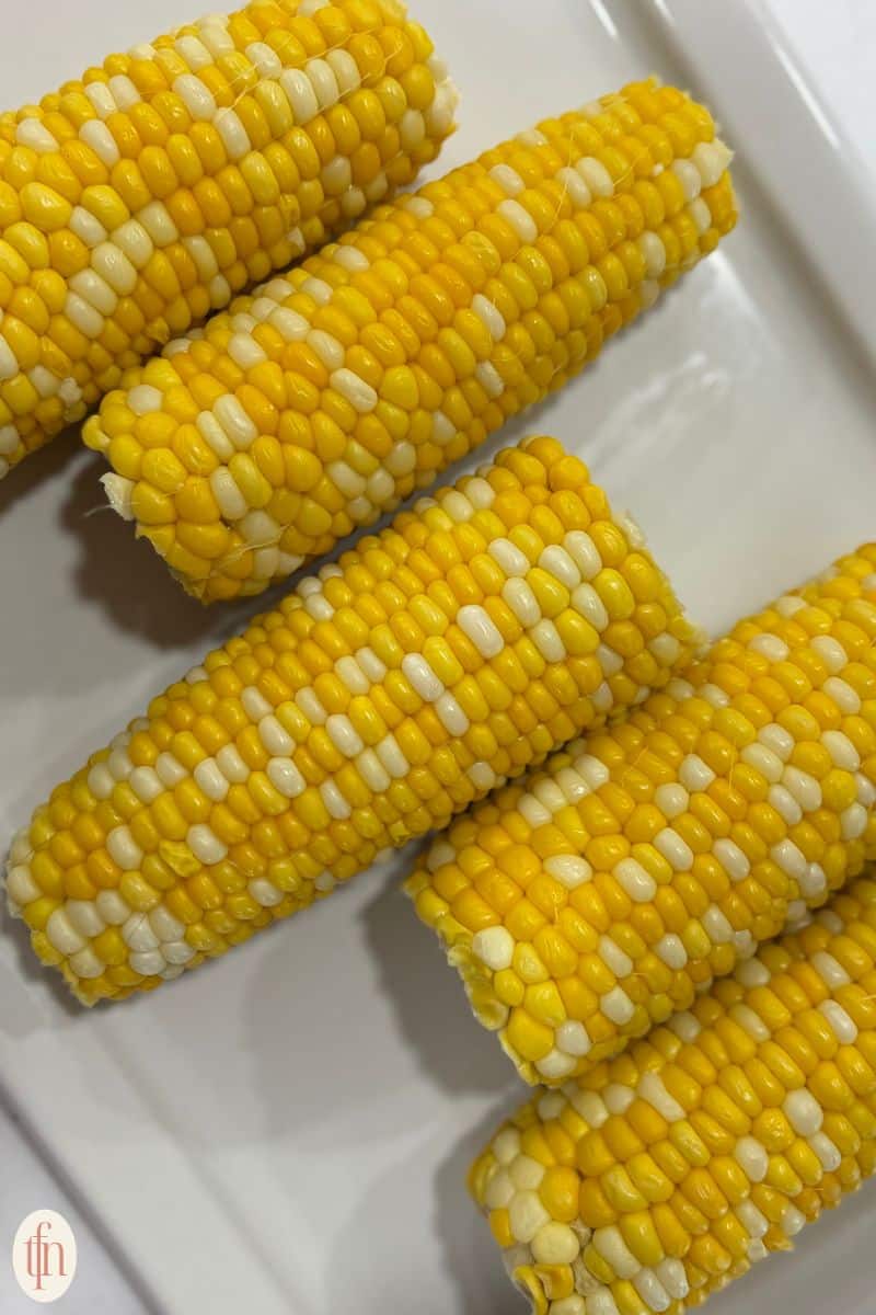 corn on the cob resting on a white serving tray.