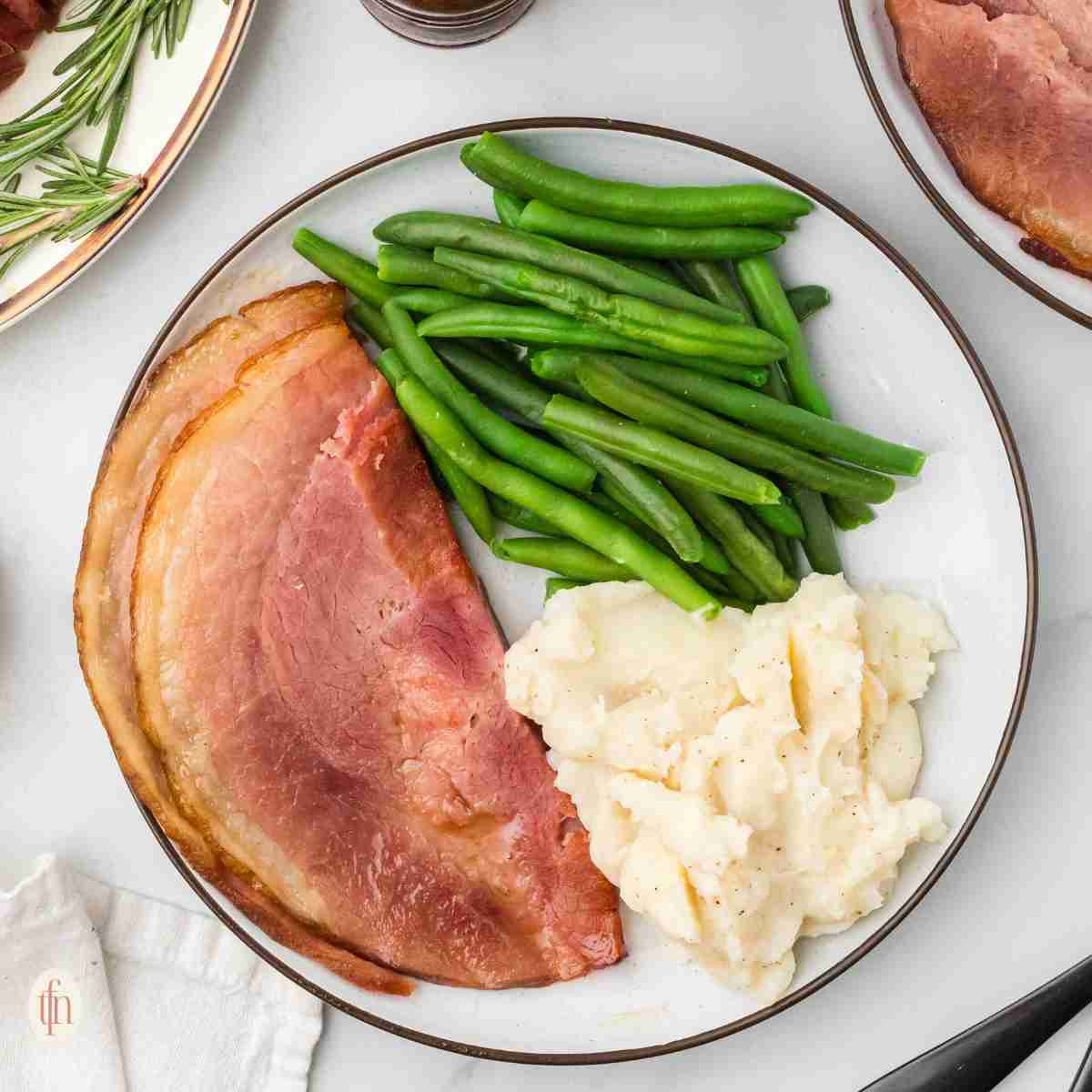 a plate with ham, mashed potatoes, and green beans.