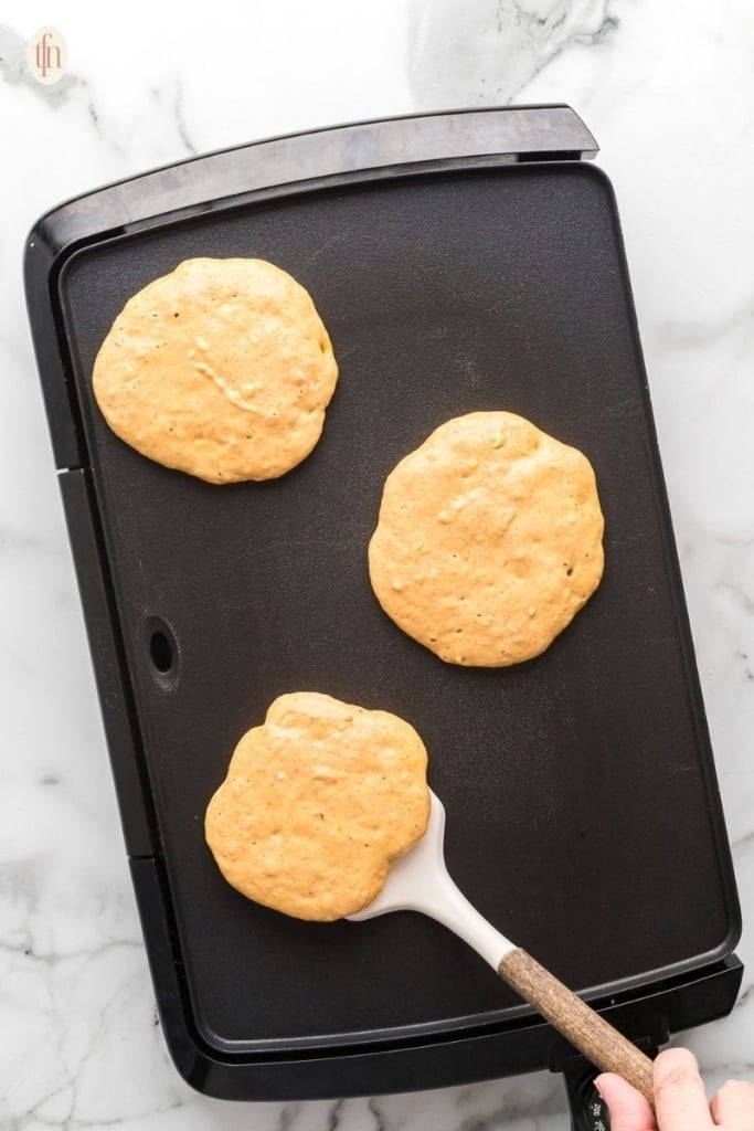 pancakes cooking on a black griddle.