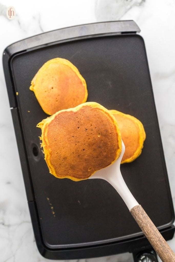pancakes cooking on a black griddle.