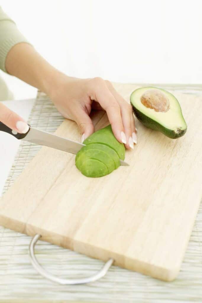 Hands slicing an avocado on a cutting board.